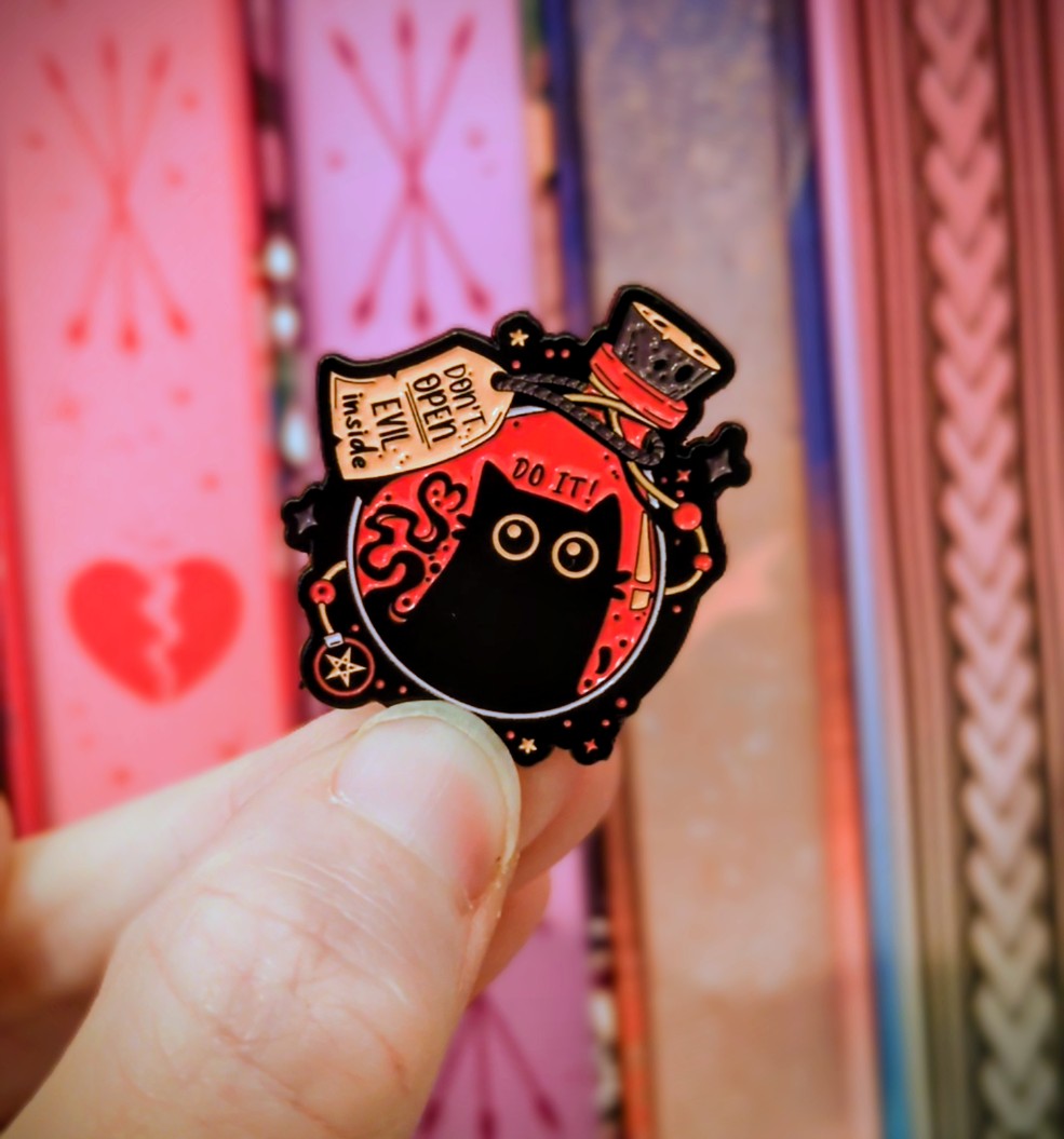 Black and pink cat-shaped pin held by a hand with a colorful background
